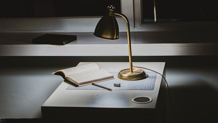 Photo of a desk with a book, lamp, and pen